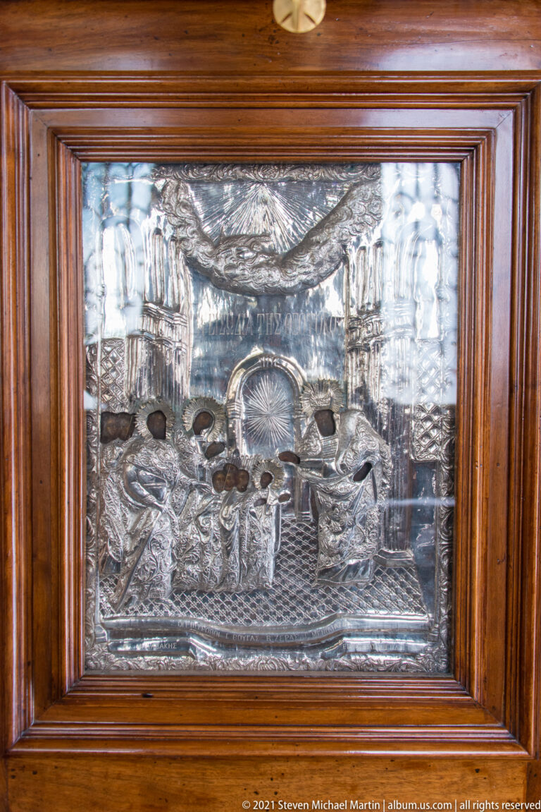 Framed embossed silver devotional panel with raised figures, architectural details, and reflective repoussé surfaces.