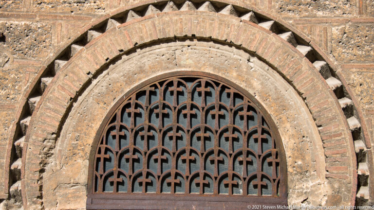 Arched Panagia Kapnikarea window with geometric iron grille, concentric brick bands, and sawtooth masonry ornament.