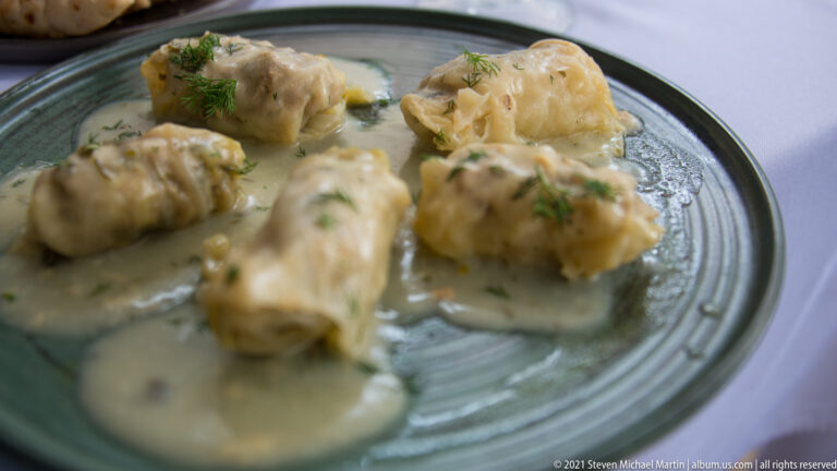 Small stuffed cabbage rolls covered in pale creamy sauce and garnished with dill on a ceramic plate.