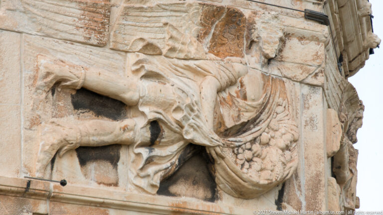 Close profile of a winged wind-deity relief with flowing drapery on the marble Tower of the Winds.