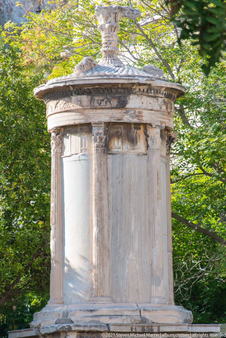 Weathered rectangular marble funerary monument with pilasters and carved cornice surrounded by dense green foliage.