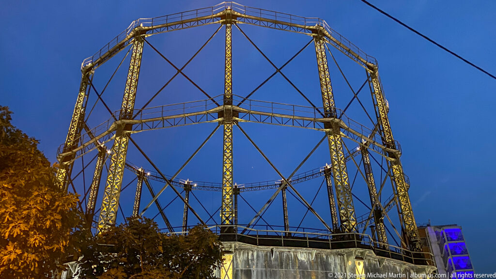 Tall circular iron gasometer framework with lattice columns and diagonal braces at Technopolis in Athens at dusk.