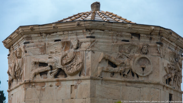Upper Tower of the Winds showing several relief figures around its octagonal marble walls beneath the tiled roof.