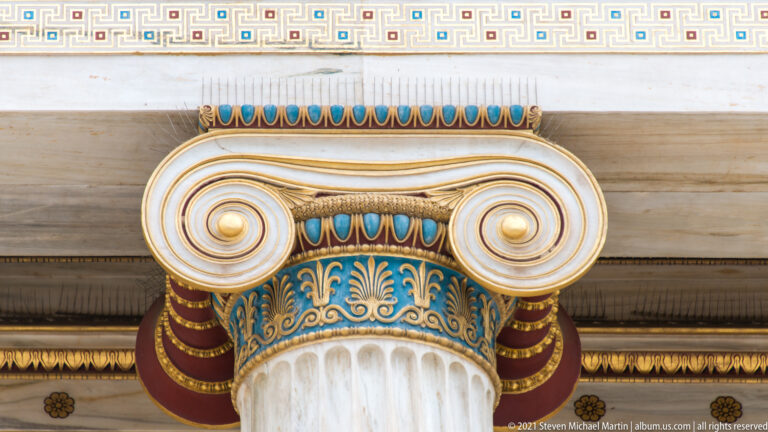 Close view of a white Ionic capital with blue, red, turquoise, and gold painted ornament at the Academy of Athens.