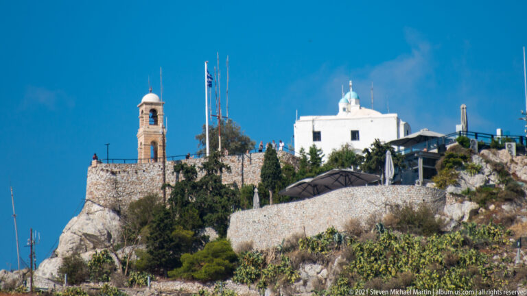 White Church of Saint George and bell tower on the rocky summit of Mount Lycabettus beneath a deep blue sky.