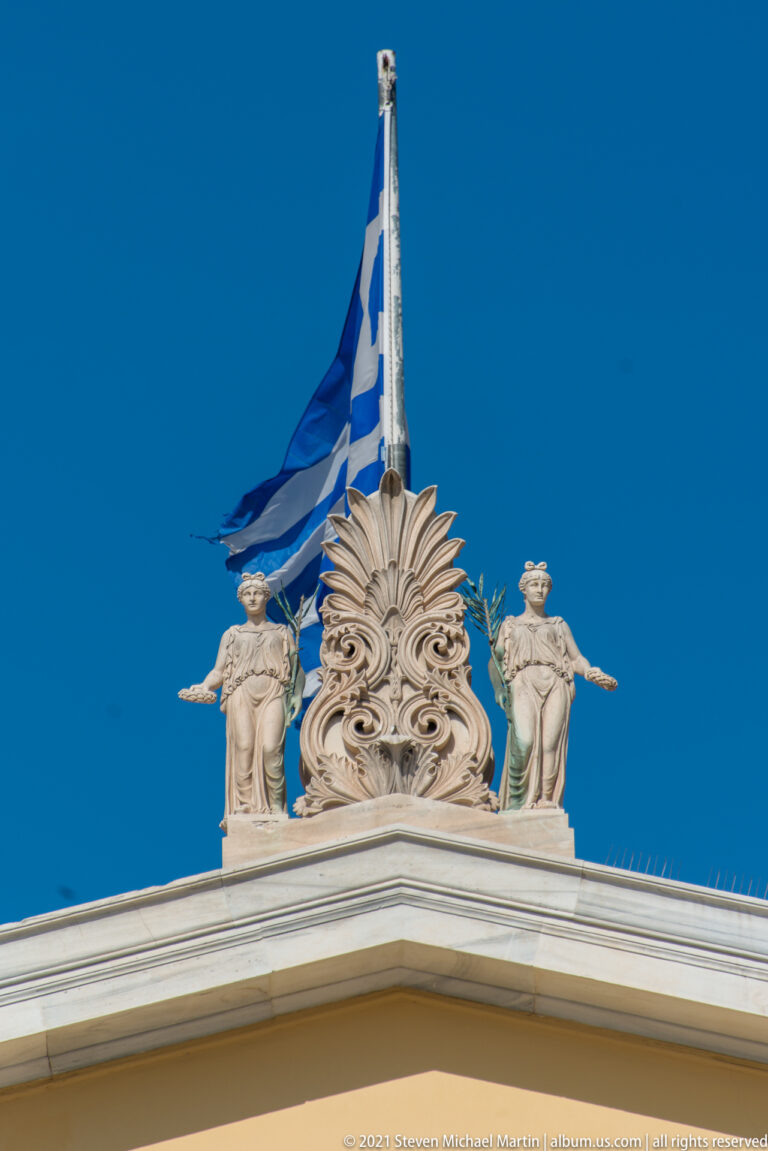 Greek flag above a carved palmette and two classical figures crowning the Zappeion roofline.