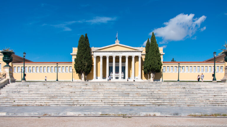 Wide view across marble steps toward the Zappeion's central Corinthian portico and long yellow façade.
