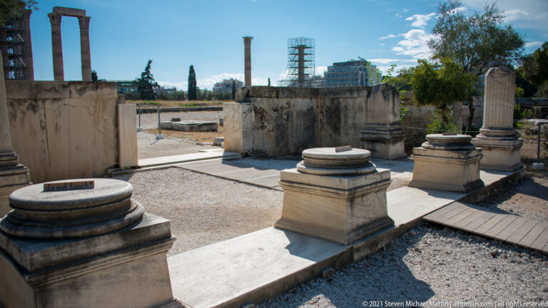 Marble column bases, pedestals, low walls, and architectural fragments within the Olympieion archaeological site.