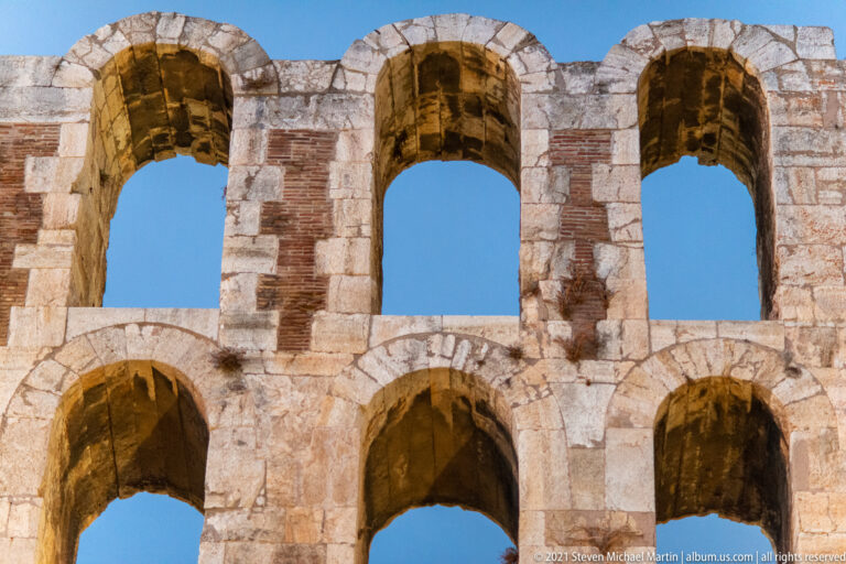 Close view of two stacked tiers of broad arches in the stone and brick stage wall of the Odeon.