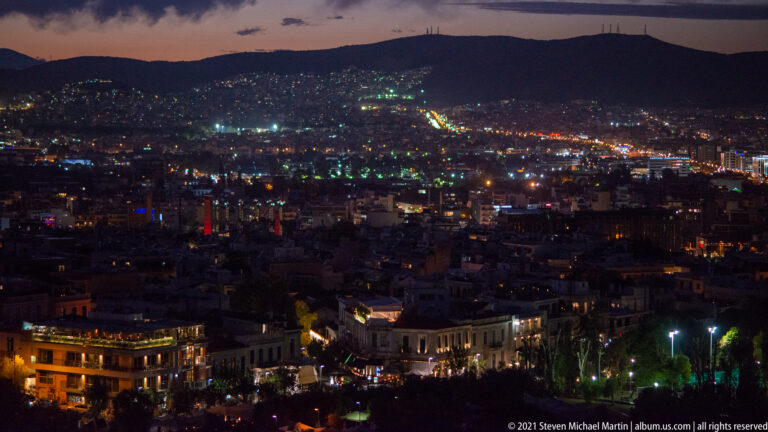 Wide night panorama of Athens filled with city lights beneath a dark mountain ridge.