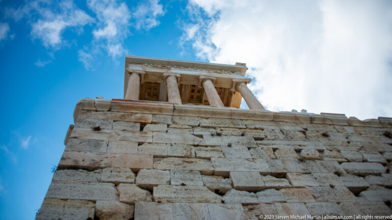 Low-angle view of the small Ionic Temple of Athena Nike above a massive stone bastion wall.