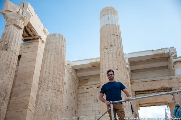 Visitor standing among tall fluted marble columns and lintels inside the Propylaea at the Acropolis entrance.