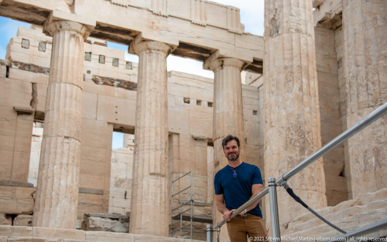 Visitor framed by weathered fluted columns, lintels, and marble walls inside the Propylaea.