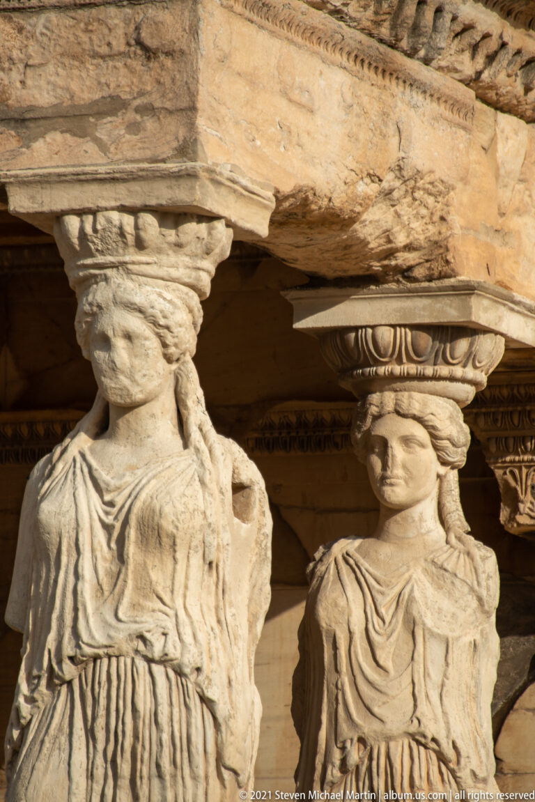 Close-up of two draped Caryatid replicas beneath the stone roof of the Erechtheion porch.