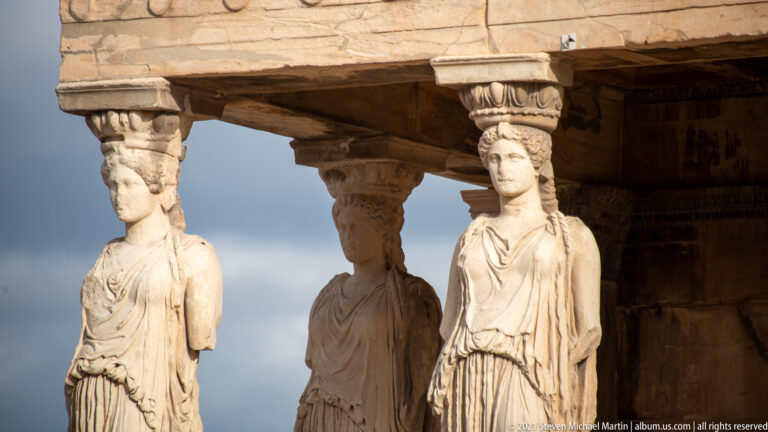 Three Caryatid replicas supporting the Erechtheion porch, seen obliquely beneath the heavy stone entablature.