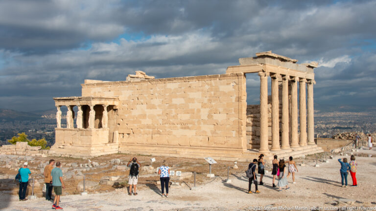 Erechtheion on the Acropolis with the Caryatid porch at left, tall Ionic columns at right, and visitors in front.