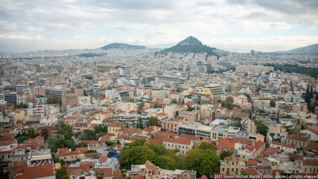 Wide view over central Athens from the Acropolis, with Mount Lycabettus rising above the dense city in the distance.