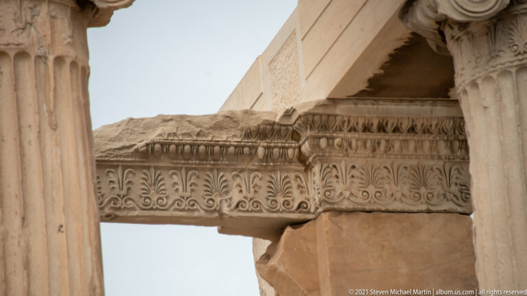 Close view of carved Ionic ornament on the Erechtheion, including a capital and decorated horizontal molding beneath plain marble blocks.