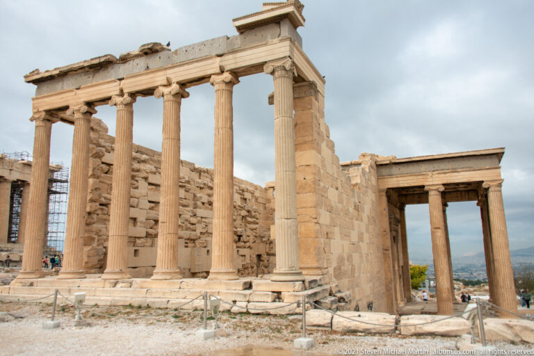 Oblique view of the Erechtheion showing the east Ionic porch, long marble wall, and an open doorway to the right.