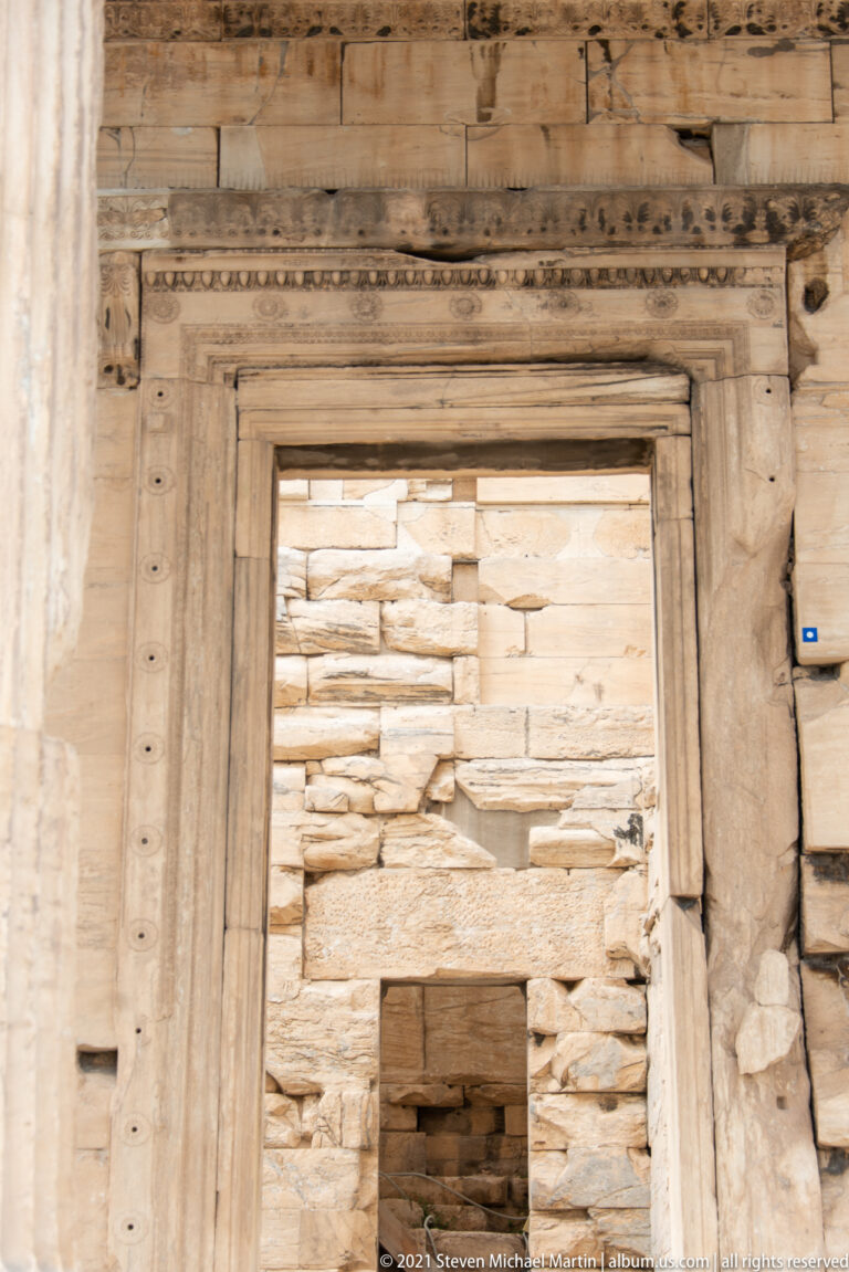 Close frontal view of a large marble doorway with layered frame, weathered lintel, and rough stone masonry visible beyond.