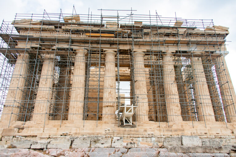 Parthenon façade covered by dense multi-level scaffolding, with Doric columns and the entablature visible through the metal framework.