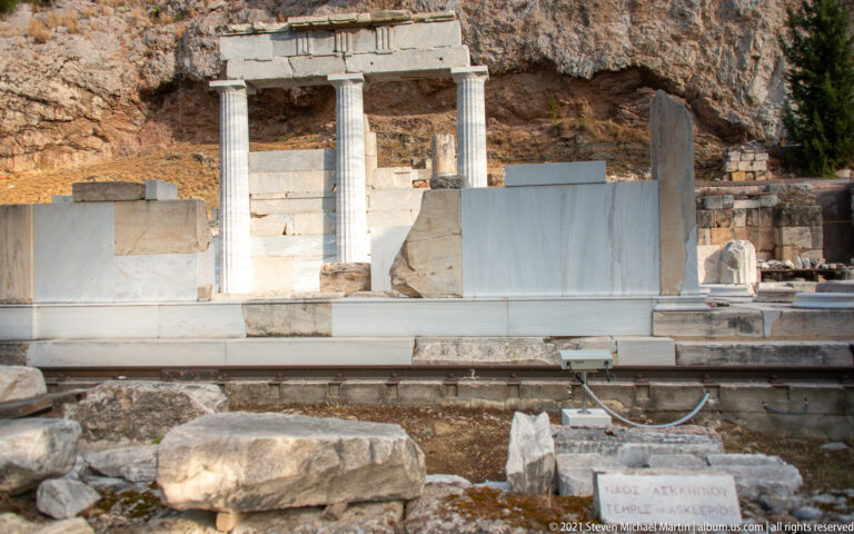 Two restored columns and an entablature among marble ruins at the foot of the Acropolis rock face.