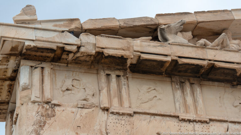 Ancient marble relief and sculptural figures set beneath a restored entablature with replacement blocks.