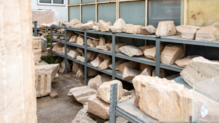 Shelves filled with pale marble blocks, carved fragments, capitals, and broken architectural pieces.