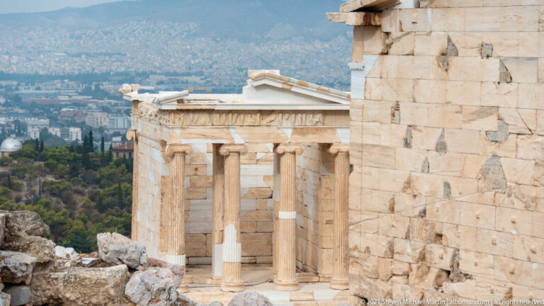 Small Ionic Temple of Athena Nike beside the Propylaia, with Athens visible in the distance.