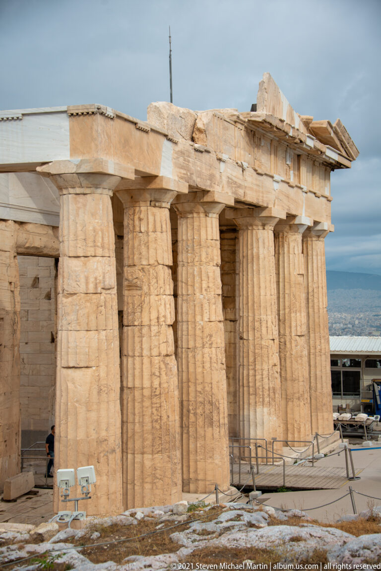 Oblique view of massive fluted Doric columns and entablature at the Propylaia under a cloudy sky.