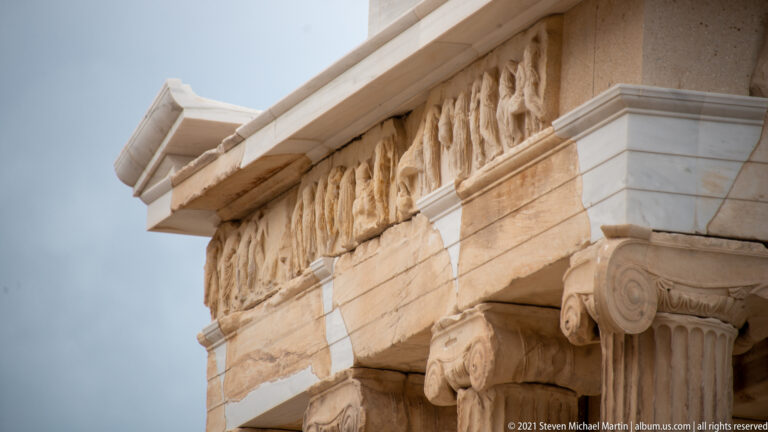 Close view of Ionic capitals, fluted columns, carved frieze, and projecting marble cornice.