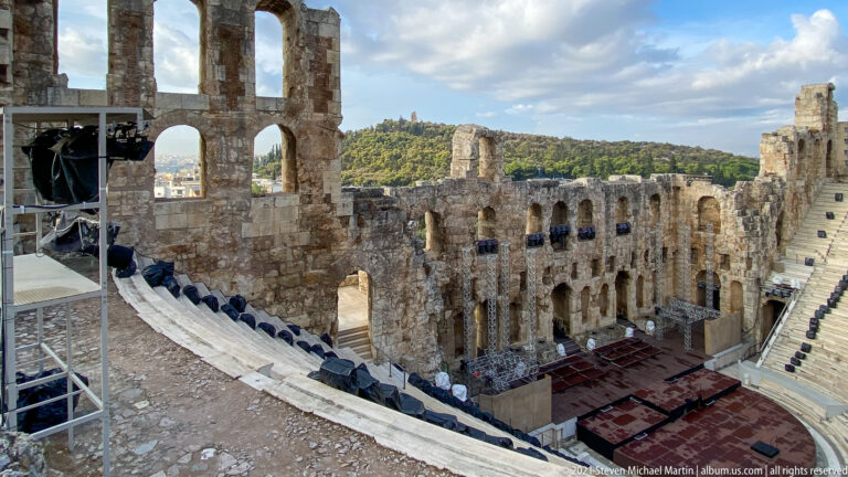 Elevated view into the Odeon of Herodes Atticus with arched stage wall and curved stone seating.