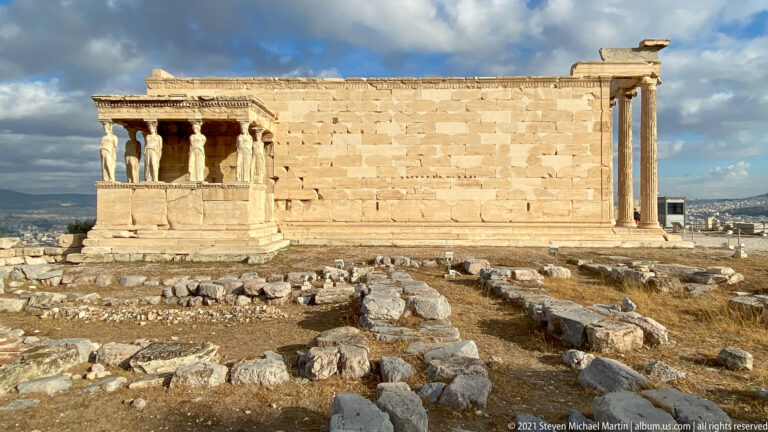 Full side view of the Erechtheion with Caryatid porch, marble wall, columns, and scattered ruins.