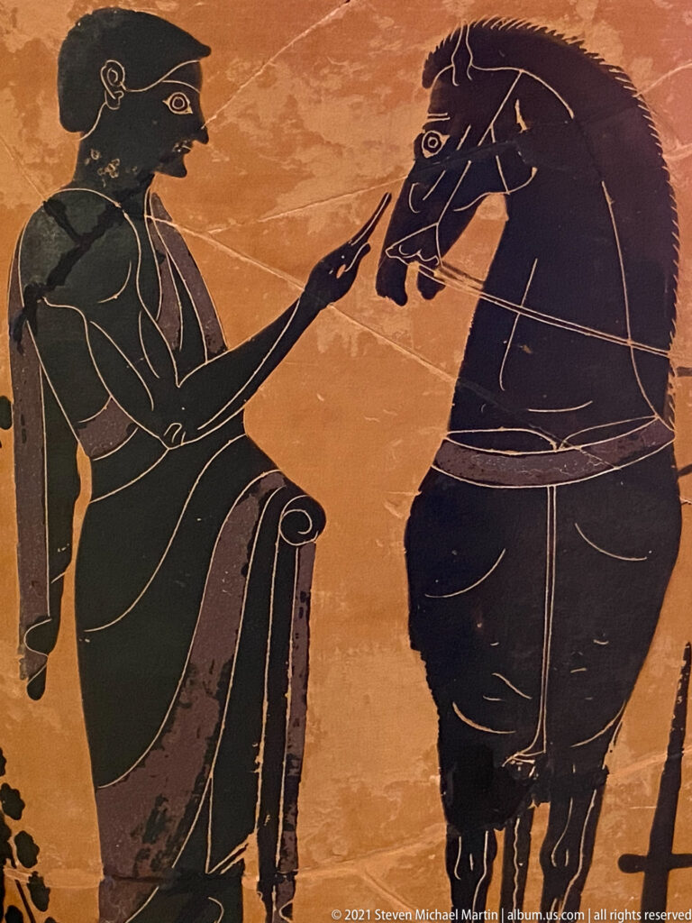 Black-figure vase detail of a standing man reaching toward the head of a large horse with an incised mane.