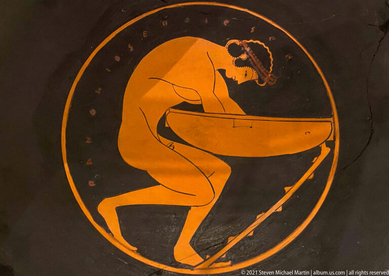 Red-figure cup tondo with a nude crouching youth leaning over a large basin-like vessel inside a circular field.
