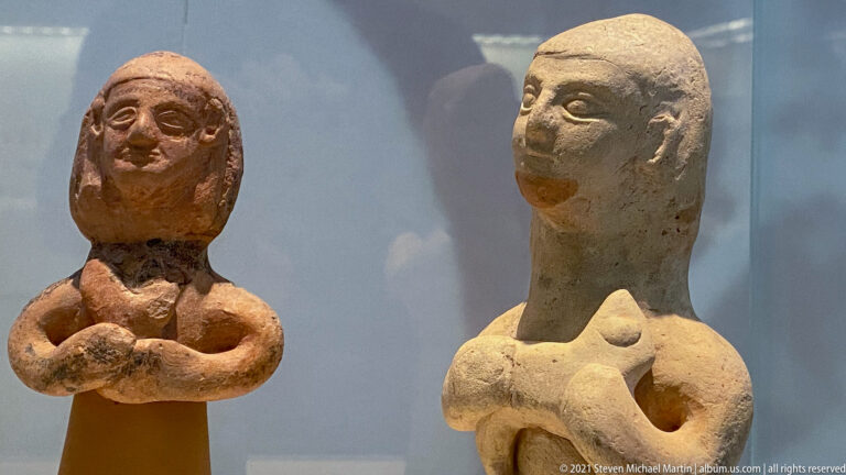Two small terracotta female busts or figurines with elongated faces and arms held across their chests.
