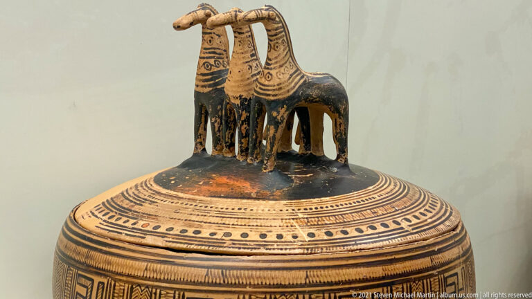 Painted ceramic lid with dense geometric bands and three standing horse figures forming a sculptural finial.