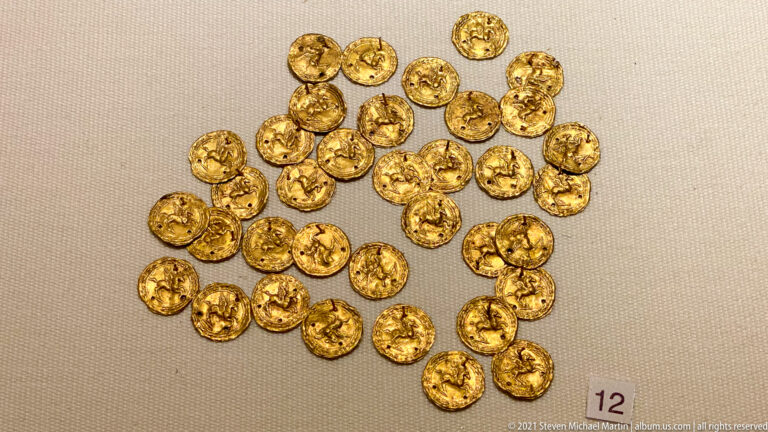 Cluster of many small circular gold disks with embossed central motifs and patterned edges.