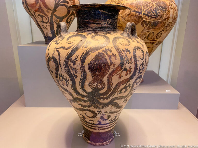 Large pale ceramic vessel with dark spirals, tendrils, and marine- or plant-like motifs covering its rounded body.