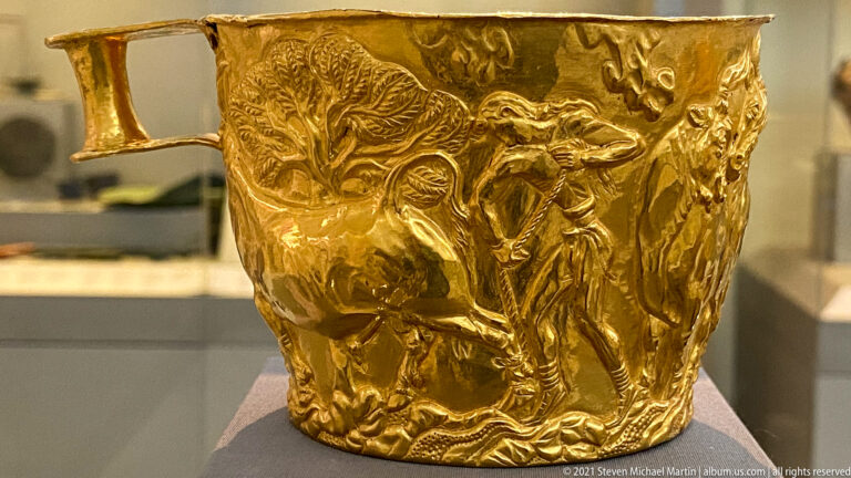 Gold Vapheio cup with a repoussé bull scene, human figures, and vegetation wrapped around the vessel wall.