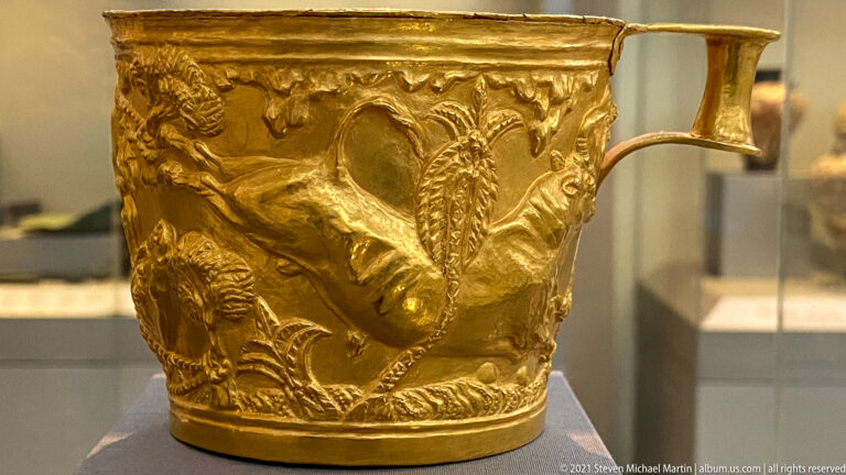 Detail of a gold Vapheio cup with a repoussé bull surrounded by trees and curling vegetation.