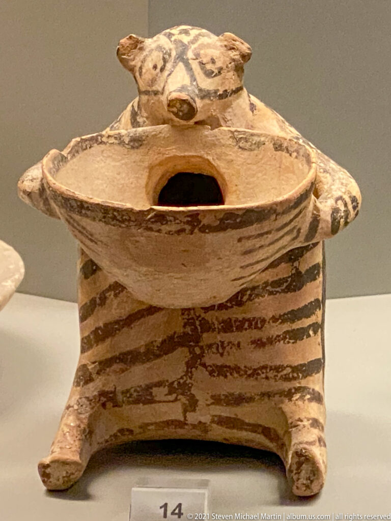 Box-like painted terracotta vessel on four feet with a domed perforated lid and projecting animal-head forms.