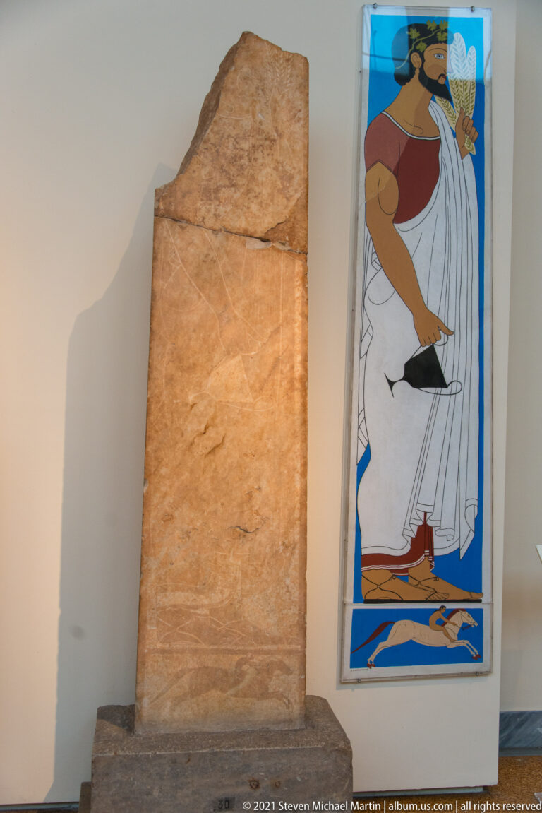 Tall weathered stone stele with faint markings beside a colorful interpretive reconstruction panel.