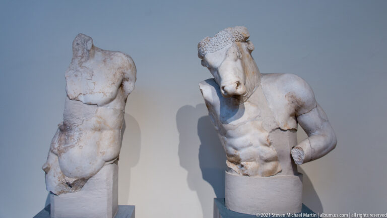 Two fragmentary marble male statues displayed side by side, one headless and both missing limbs.
