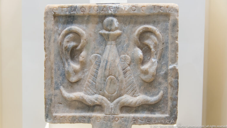 Rectangular carved stone panel with a central stylized motif, paired volutes, and inscriptions along the borders.