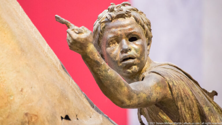 Close view of the young bronze rider from the Jockey of Artemision with tousled hair and one arm reaching forward.