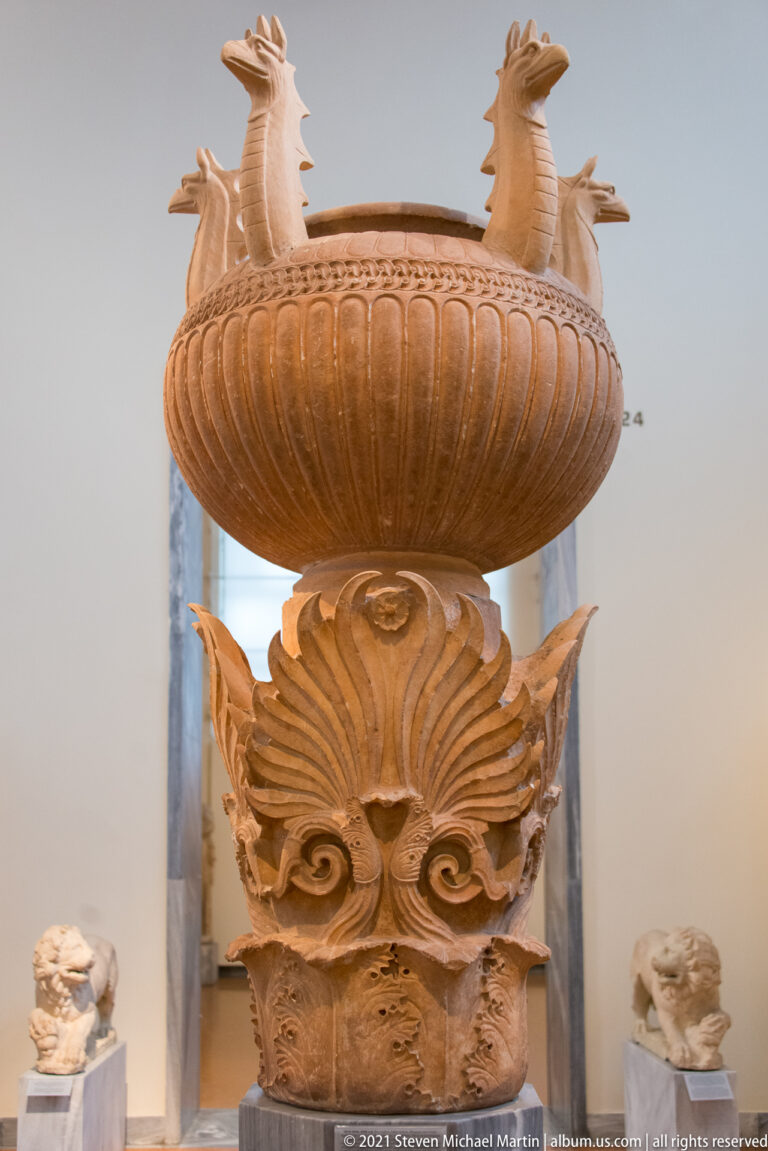 Large fluted stone bowl on an elaborate vegetal support, with paired projecting animal-like forms above the rim.