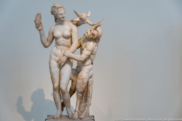 Marble group of a standing nude woman with a smaller male companion and a small creature or attribute near her shoulder.