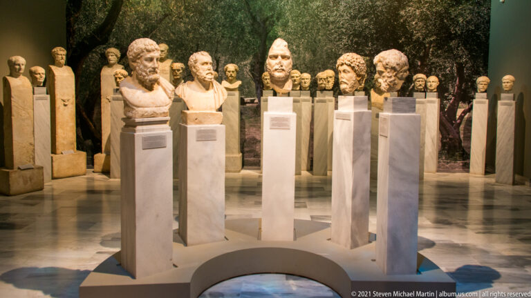 Ancient portrait heads and busts on tall pedestals, viewed across a warmly lit museum gallery.
