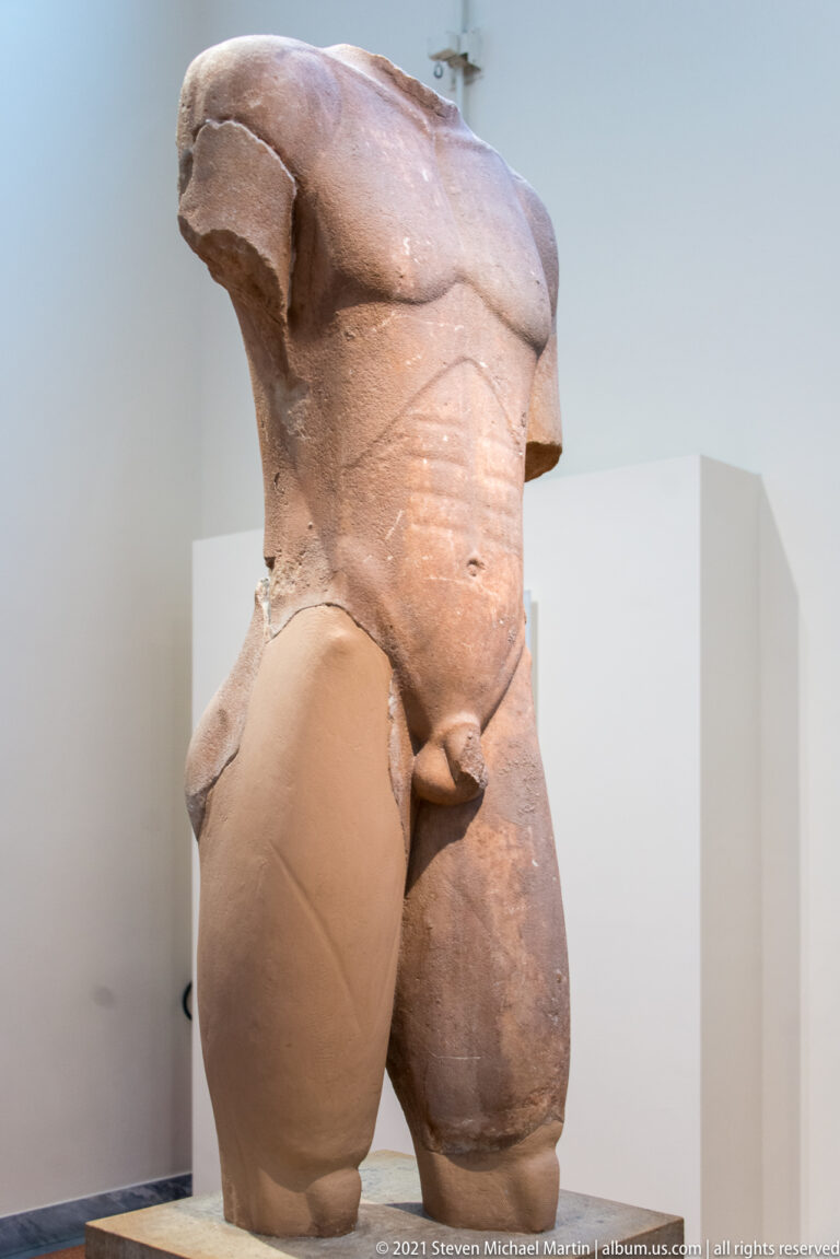 Fragmentary stone male torso and thighs from a monumental nude statue.